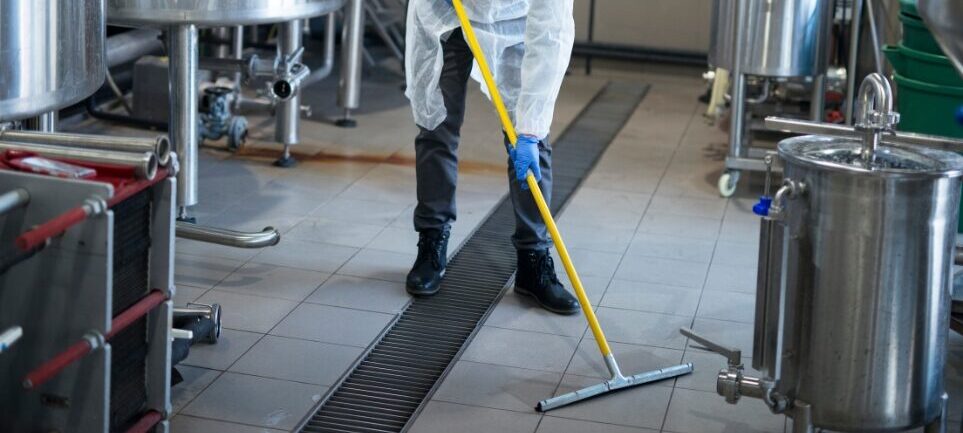 Worker cleaning floor with protective equipment and mop.